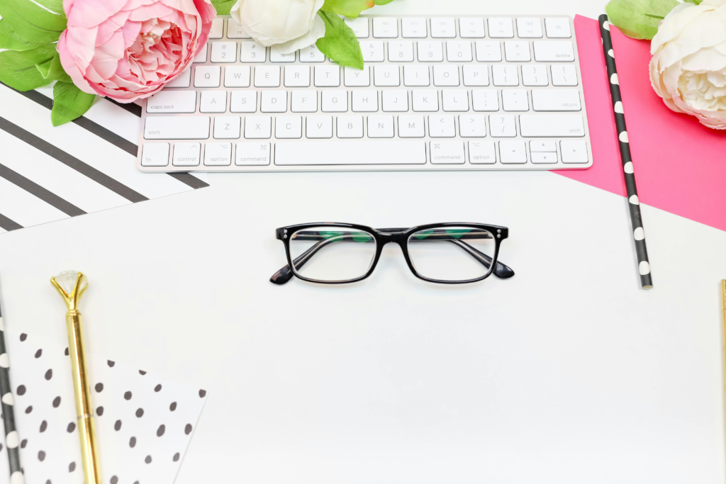 A modern feminine workspace with eyeglasses, keyboard, and flowers, creating an elegant and contemporary office vibe.